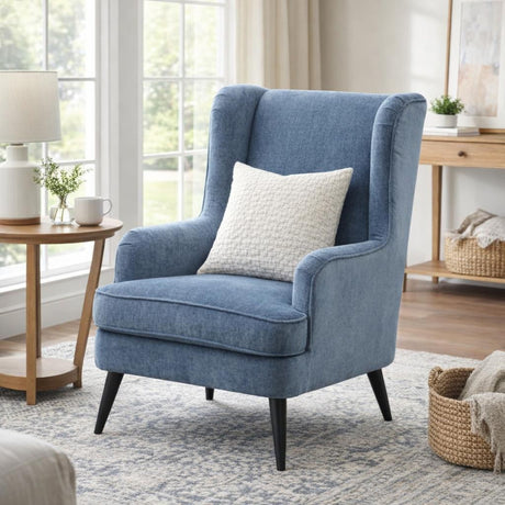 Hill Interiors blue wingback armchair with high curved sides, cushioned seat and dark tapered legs, styled with a woven cushion in a bright living room.