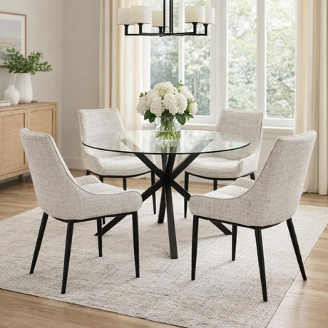 Hill Interiors Vestamby round glass dining table with clear tempered top and black crossed base, styled with cream upholstered chairs in a bright dining room.