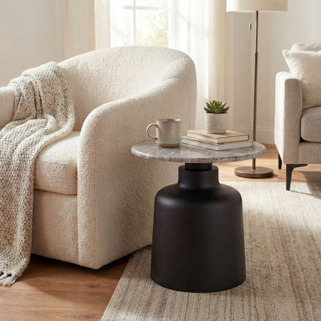 Hill Interiors Themworth round side table with grey marble-effect top and black metal base, styled beside a bouclé armchair in a neutral living room.