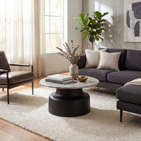Hill Interiors Themworth round coffee table with marble-effect top on a black pedestal base, styled with books and eucalyptus in a bright living room.