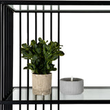 Hill Interiors Glass Shelf Unit with Black Metal Frame styled with a potted green plant and ribbed grey tealight holder on a clear tempered glass shelf.