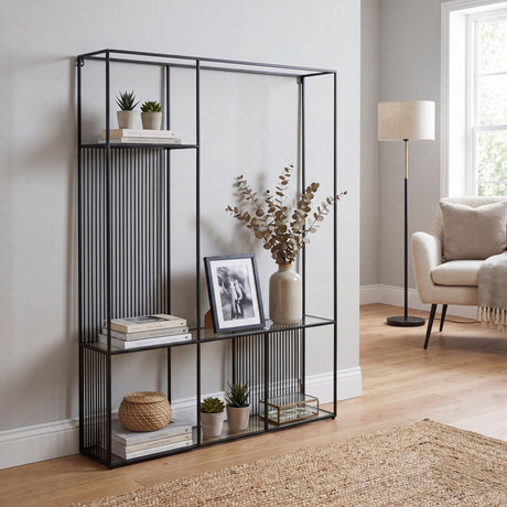 Hill Interiors Glass Shelf Unit with slim black metal frame and clear glass shelves, styled with books, plants and a framed photo in a living room.