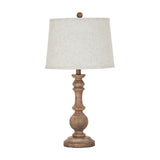 Hill Interiors Velantha table lamp with a sculptural brown resin candlestick base and tapered edged linen shade, shown on a plain white background.