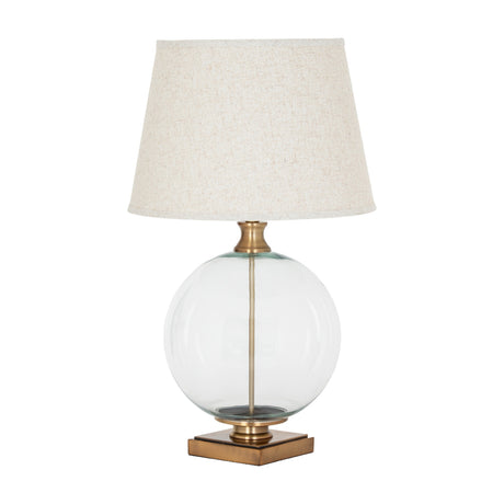 Hill Interiors Glass Orb Table Lamp with clear round base, brass-finished detailing and tapered natural linen shade with edged trim on white.