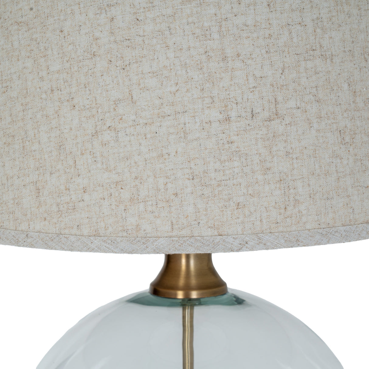 Close-up of the Hill Interiors Glass Orb Table Lamp showing the brass-finished neck joining the clear glass base to the edged natural linen shade.