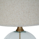 Close-up of the Hill Interiors Glass Orb Table Lamp showing the brass-finished neck joining the clear glass base to the edged natural linen shade.