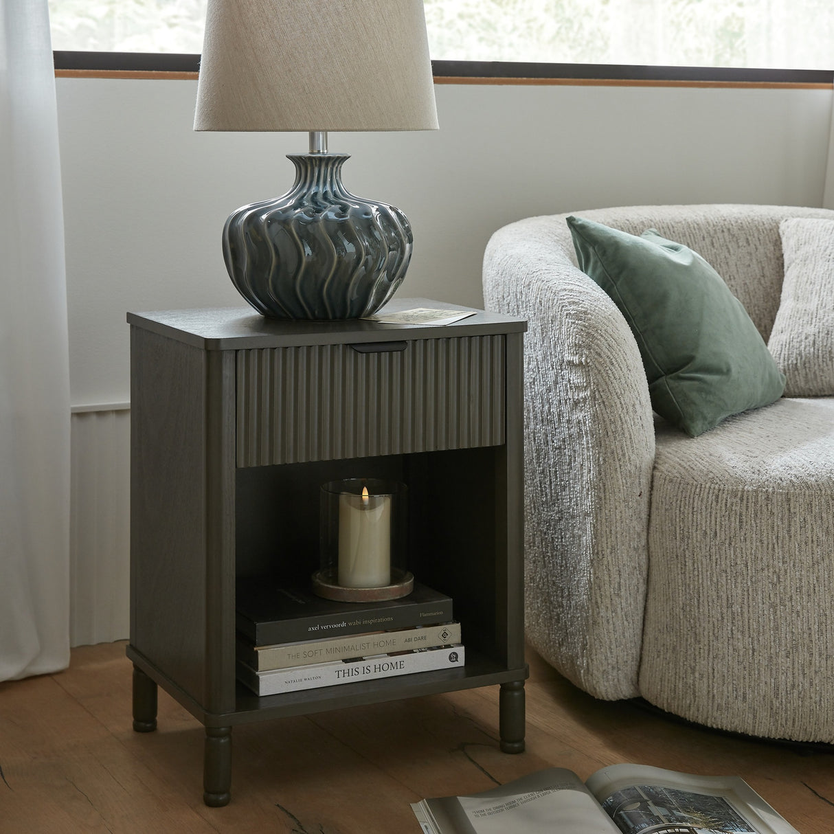 Hill Interiors ceramic table lamp with a textured dark glazed base and natural linen shade, styled on a fluted nightstand beside a bouclé sofa.
