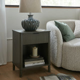Hill Interiors ceramic table lamp with a textured dark glazed base and natural linen shade, styled on a fluted nightstand beside a bouclé sofa.