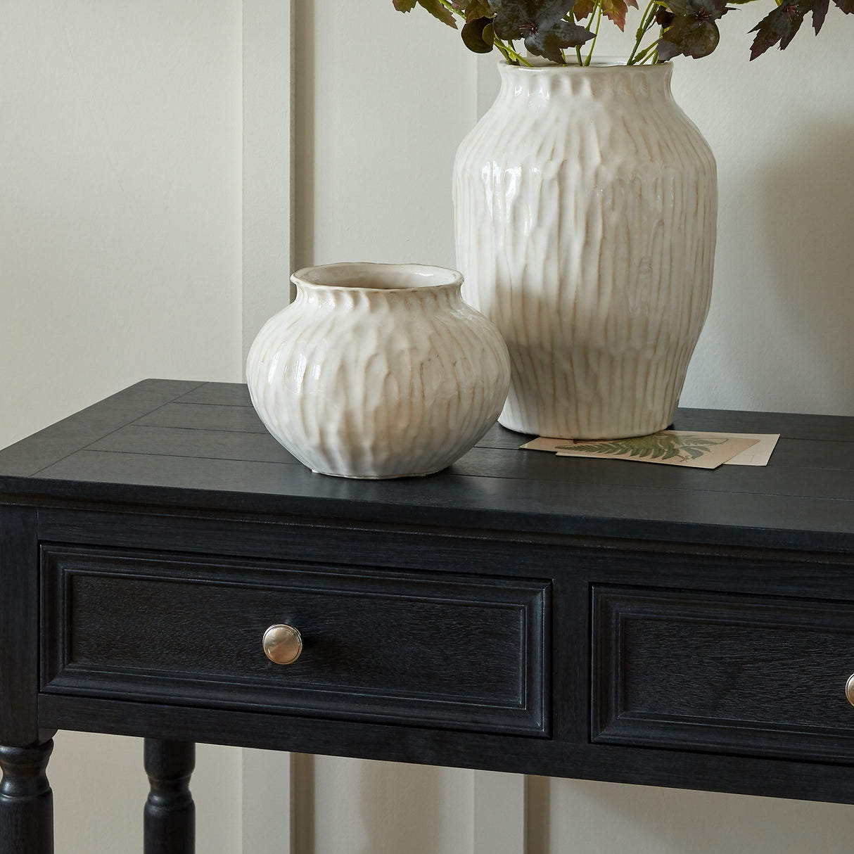 Hill Interiors Squat Ceramic Vase in white with a rounded textured body, shown on a black console table beside a taller matching vase holding stems.