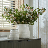 Hill Interiors Wide Hewn ceramic vases in white with textured rounded bodies, the larger filled with white blossom branches on a wooden sideboard by a window.