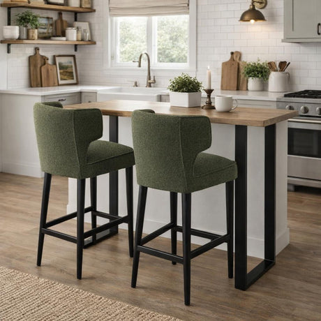 Pair of Hill Interiors Quennomer green boucle barstools with black wooden legs at a wood-topped kitchen island in a bright farmhouse-style kitchen.