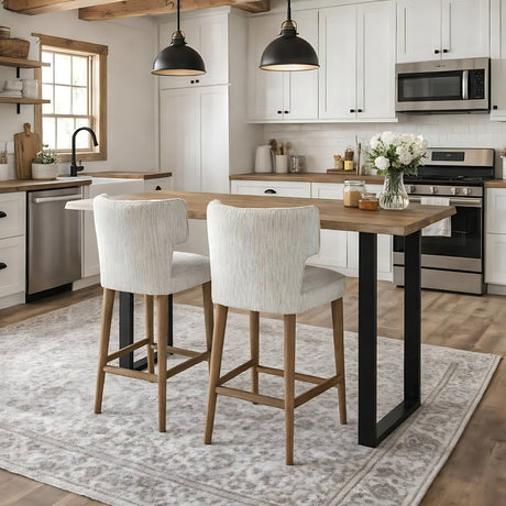 Hill Interiors Quennomer bar stools in grey textured upholstery with wooden legs, set at a wood and black metal island in a white farmhouse kitchen.