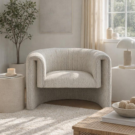 Hill Interiors Quennomer accent armchair in soft grey upholstery with a curved wraparound back, styled in a sunlit living room with a side table and plant.