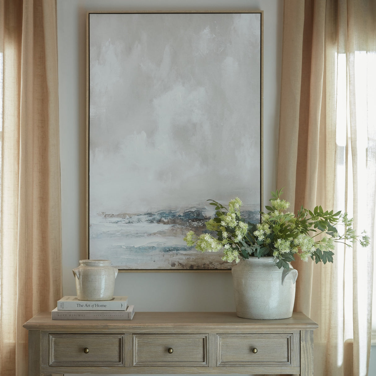Hill Interiors hand painted canvas in a slim wooden frame, showing a muted abstract landscape in grey, blue and brown, hung above a wooden console.
