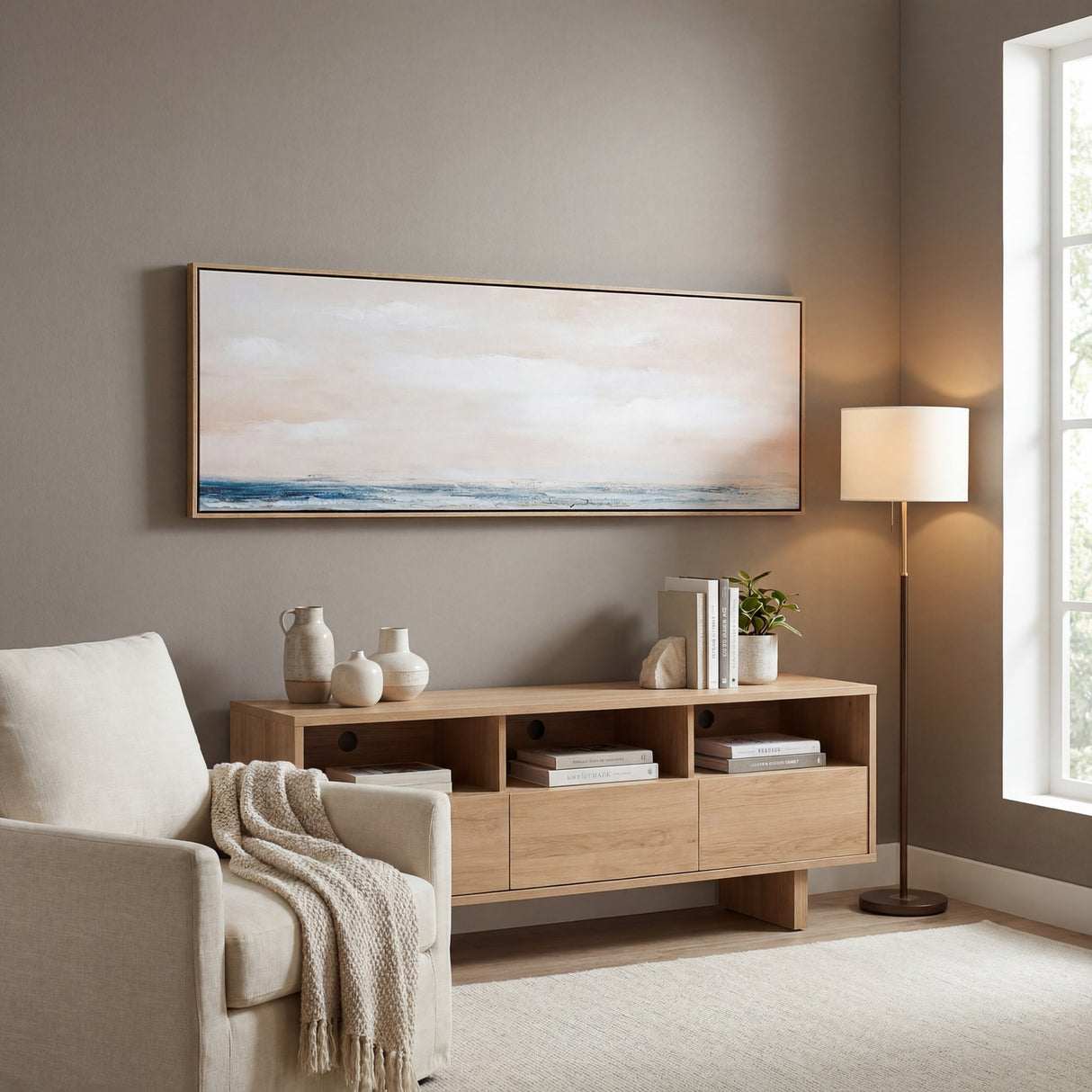 Hill Interiors hand painted landscape canvas in slim wooden frame with soft pink sky and blue sea, hung above a light oak sideboard in a living room.