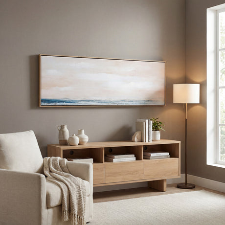 Hill Interiors hand painted landscape canvas in slim wooden frame with soft pink sky and blue sea, hung above a light oak sideboard in a living room.