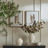 Hill Interiors framed wall art in wooden frames displayed above a dark sideboard with cream vases, foliage stems and stacked books in a neutral living space.