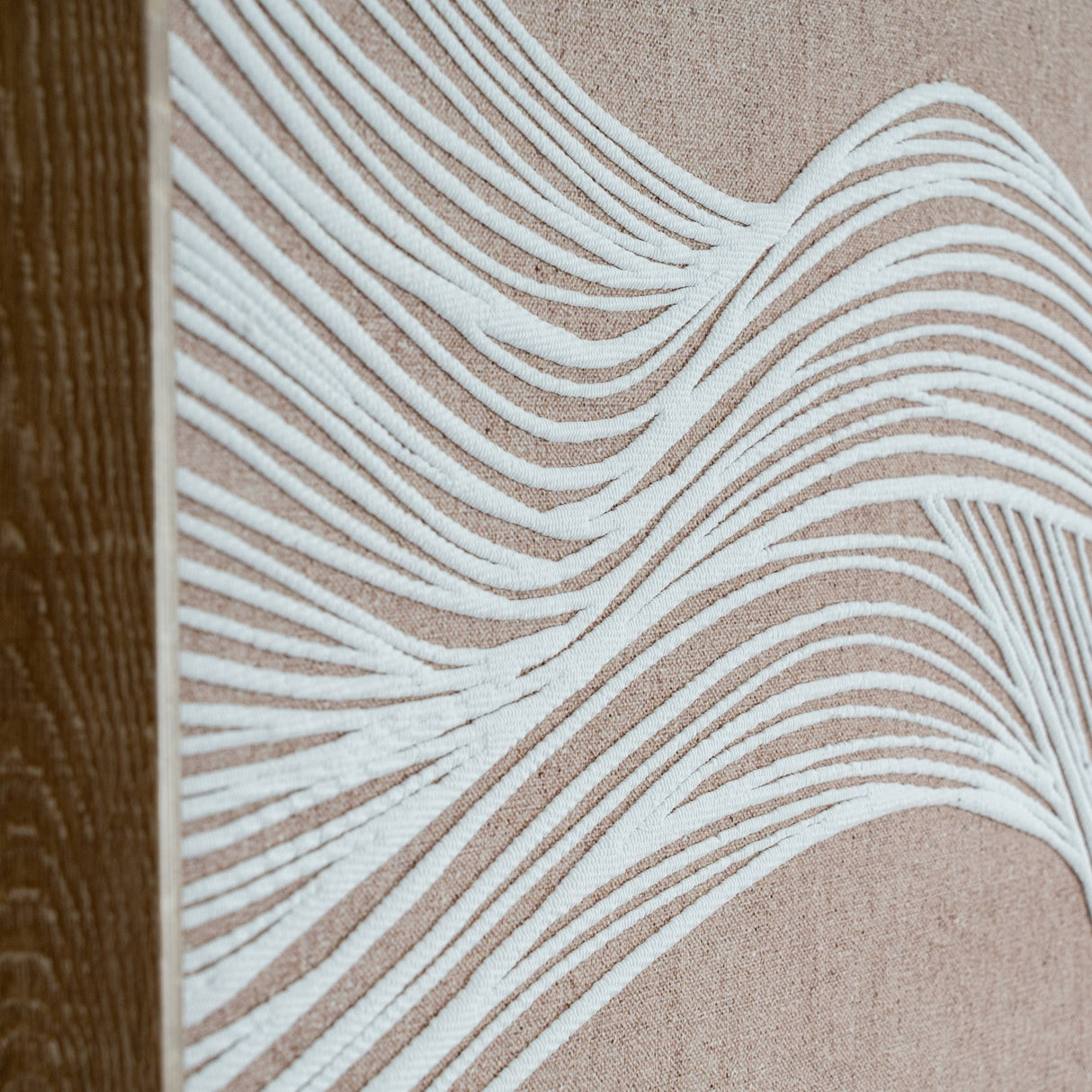 Close-up of Hill Interiors Line Art Framed Wall Print in Brown, showing white flowing line detail on neutral fabric beside the warm brown wooden frame.