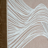 Close-up of Hill Interiors Line Art Framed Wall Print in Brown, showing white flowing line detail on neutral fabric beside the warm brown wooden frame.