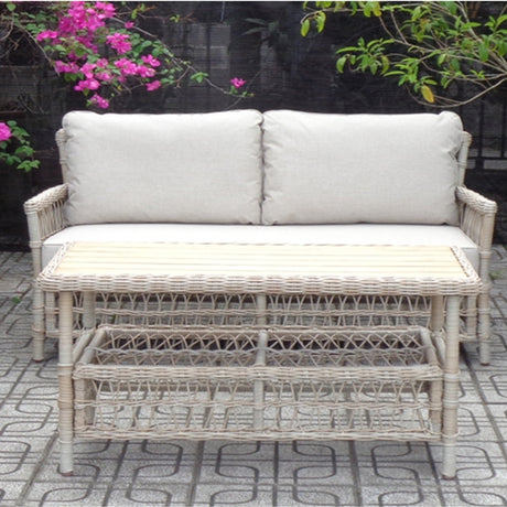 Hill Interiors Rattan Four-Seater Garden Lounge Set in beige with woven sofa, cushioned back, and matching low table on a patio by pink blossoms.