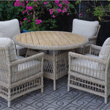Hill Interiors outdoor 4 seater dining set with round plank-top table and four beige woven armchairs with cushions on a patio by flowering shrubs.