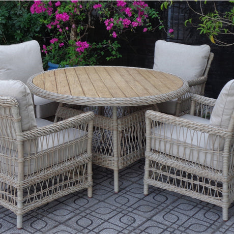 Hill Interiors outdoor 4 seater dining set with round plank-top table and four beige woven armchairs with cushions on a patio by flowering shrubs.