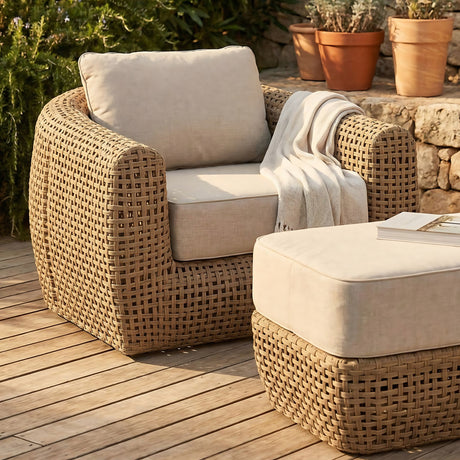 Hill Interiors Rattan Garden Lounge Chair in brown with cream cushions and throw, paired with a matching ottoman on decking beside terracotta planters.