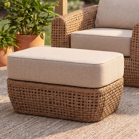 Hill Interiors Outdoor Footstool in woven brown metal with a beige cushion, set on a patio rug beside a matching lounge chair and potted plants.