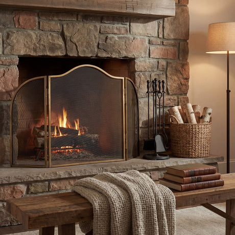 Hill Interiors Brass Fire Screen with arched mesh panels set before a lit stone fireplace, alongside a companion set, birch log basket and floor lamp.