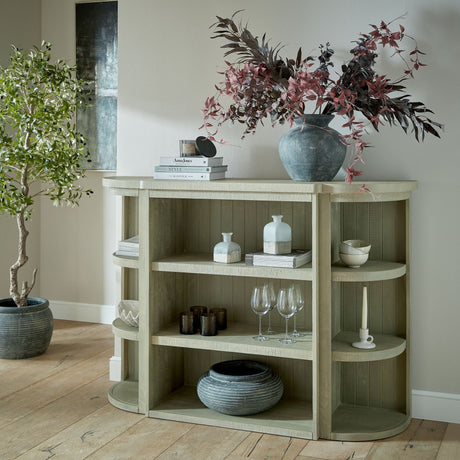 Hill Interiors 3-Shelf Wooden Storage Unit in grey styled in a living room with vases, glassware and books, beside an olive tree and abstract artwork.