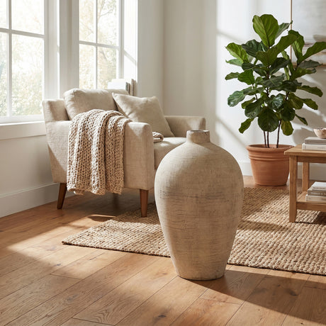 Hill Interiors Large Ceramic Vase in cream with a rounded body and tapered neck, placed on a jute rug beside a linen armchair in a sunlit living room.