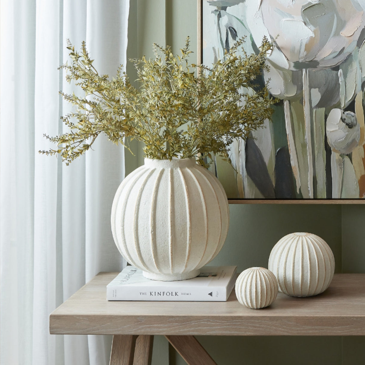 Hill Interiors ceramic globe vase in white with vertical ribbed detail, holding dried golden foliage on a console table beside two matching decorative spheres.