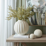 Hill Interiors ceramic globe vase in white with vertical ribbed detail, holding dried golden foliage on a console table beside two matching decorative spheres.