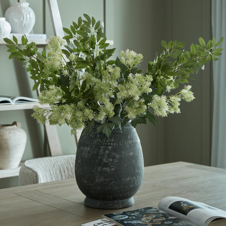 Hill Interiors Etched Tall Ceramic Vase in black with rounded body and textured pattern, holding white flowering stems on a wooden table in a living room.