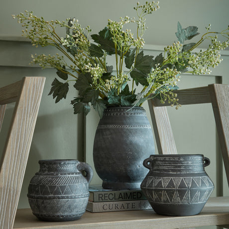 Hill Interiors Etched Ceramic Jug in black displayed with two matching etched pots on a wooden shelf, holding tall foliage and white berry stems.
