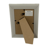 Back view of the Hill Interiors white wooden 4x6in photo frame showing MDF backing, triangular hanging hooks, kickstand, and warning label.