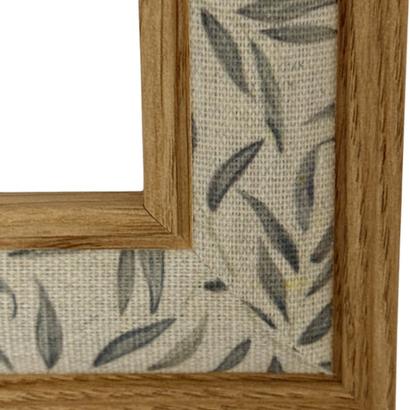 Close-up of Hill Interiors Wooden Photo Frame in brown, showing the solid wood corner moulding and grain against a leaf-patterned linen backing.