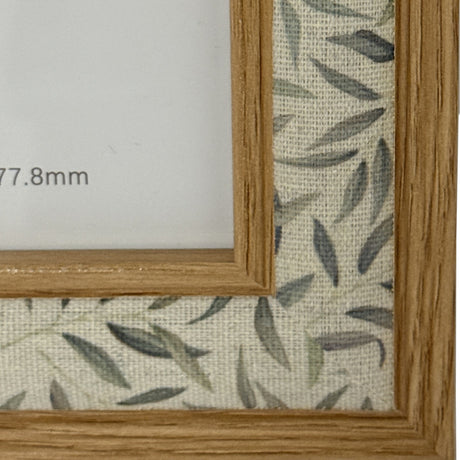 Close-up of Hill Interiors Wooden Photo Frame 5x7in in brown, showing the grained wood profile against a leaf-patterned linen backing.