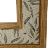 Close-up corner detail of the Hill Interiors Wooden Photo Frame in brown, showing the visible timber grain against leaf-patterned linen fabric backing.