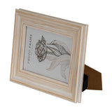 Hill Interiors wooden 4x6 photo frame in soft white with visible grain, angled view showing kickstand back and floral sample print on a white background.