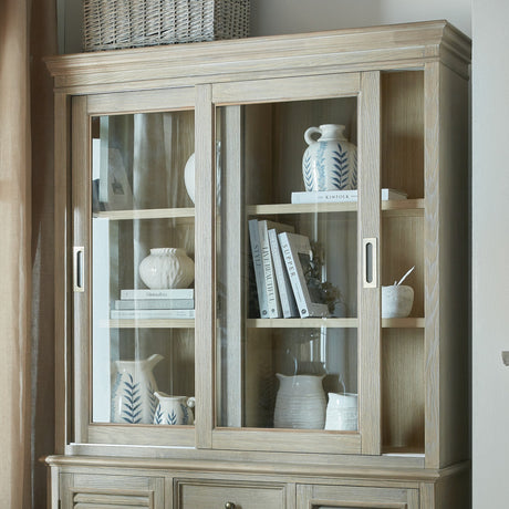 Hill Interiors Sliding Glass Dresser Top Cabinet in brown wood, styled with ceramics and books behind sliding glass doors, topped with woven baskets.