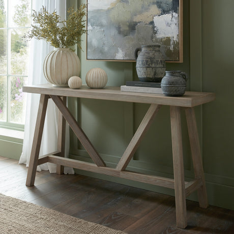 Hill Interiors Wooden Console Table in brown with A-frame trestle legs, styled with vases and artwork against a sage green wall in a hallway setting.