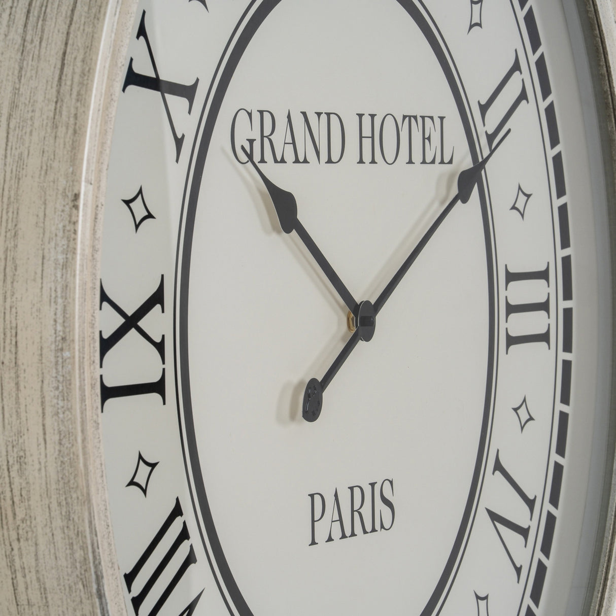 Close-up of Hill Interiors Large Round Wall Clock with grey wooden frame, glass face, Roman numerals, black hands, and Grand Hotel Paris lettering.