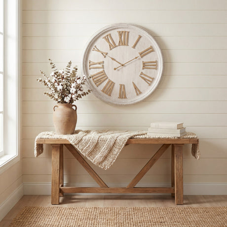 Hill Interiors White Wash Wooden Wall Clock with raised Roman numerals above a rustic wooden bench styled with cotton stems and books.