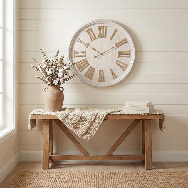 Hill Interiors White Wash Wooden Wall Clock with raised Roman numerals above a rustic wooden bench styled with cotton stems and books.