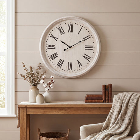 Hill Interiors white wash wooden wall clock with black Roman numerals, mounted above a rustic console table with vases and books in a neutral living room.