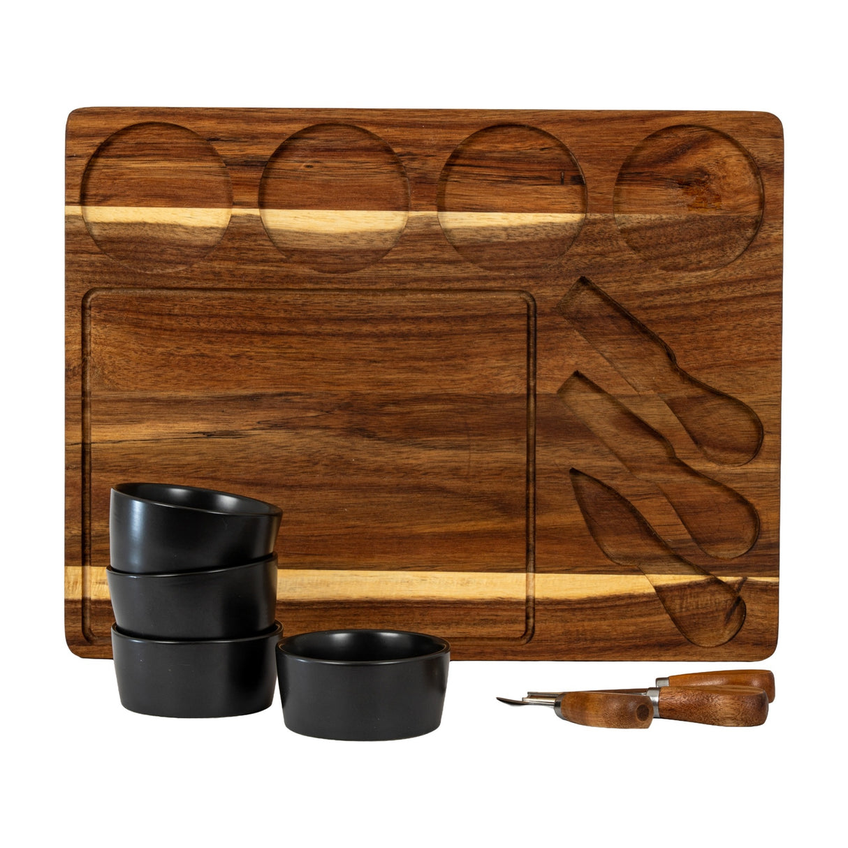 Hill Interiors acacia cheese board with carved recesses for bowls and knives, shown with four black ceramic bowls and wooden-handled cutlery.