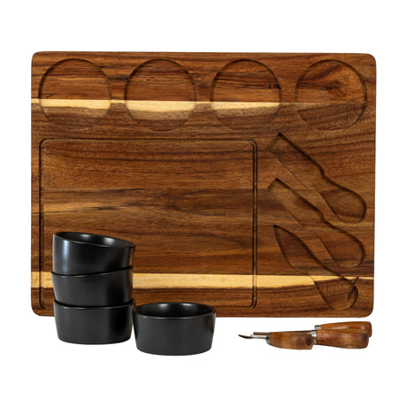 Hill Interiors acacia cheese board with carved recesses for bowls and knives, shown with four black ceramic bowls and wooden-handled cutlery.