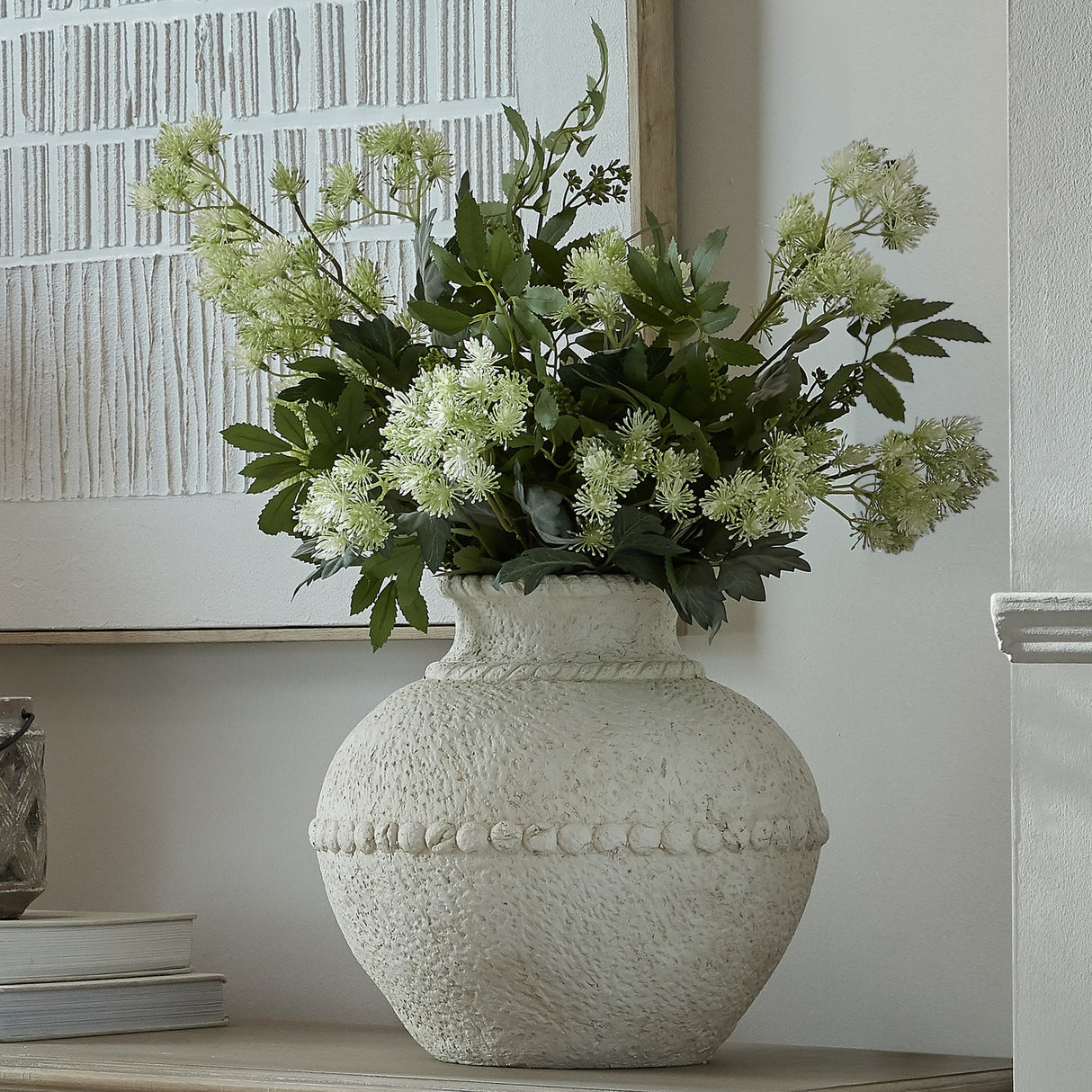 Hill Interiors medium stone-effect ceramic vase in white with textured beaded band, holding green foliage and blooms on a sideboard beside framed art.