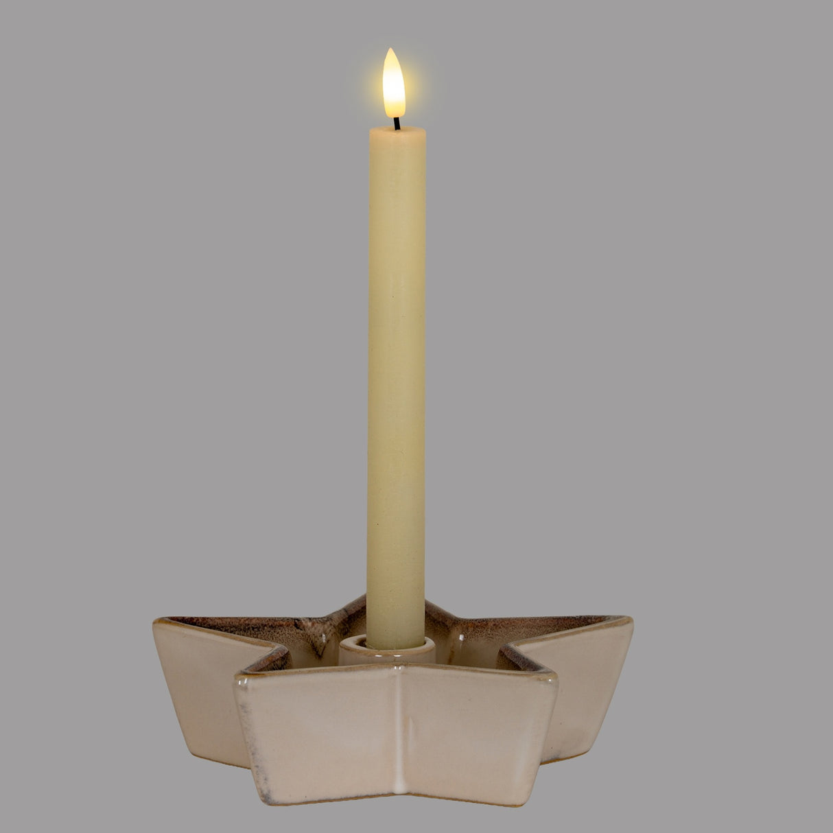 Hill Interiors Small Cement Star Candle Holder in white, holding a single lit ivory taper candle, shown against a plain grey background.